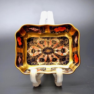 Peut inclure: Un plat rectangulaire en porcelaine présentant un fond bleu foncé avec un filigrane doré complexe, des motifs floraux orange et un motif floral central symétrique. Les bords sont festonnés et dorés, avec un design en treillis détaillé.