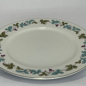 May include: A white ceramic dinner plate with a gold rim and a green and purple floral design around the edge.