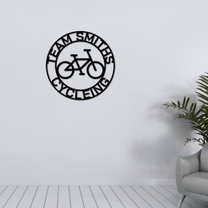 May include: Black metal wall decor with the text "Team Smiths Cycling" in a circle with a bicycle silhouette inside.