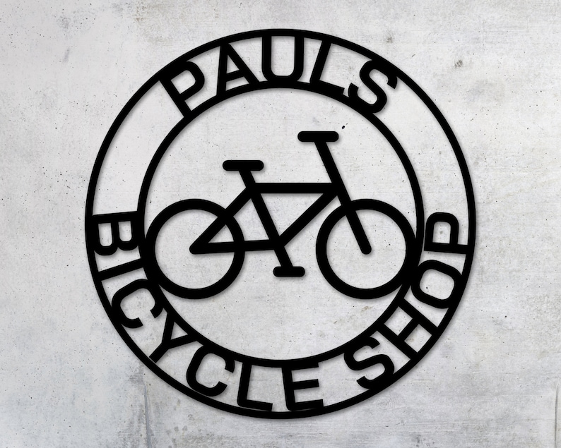 May include: Black and white circular sign with the text "Paul's Bicycle Shop" around the edge. A bicycle silhouette is in the center of the sign.