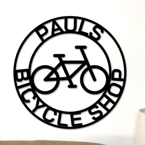 May include: Black and white circular sign with the text "Paul's Bicycle Shop" and a silhouette of a bicycle inside the circle.