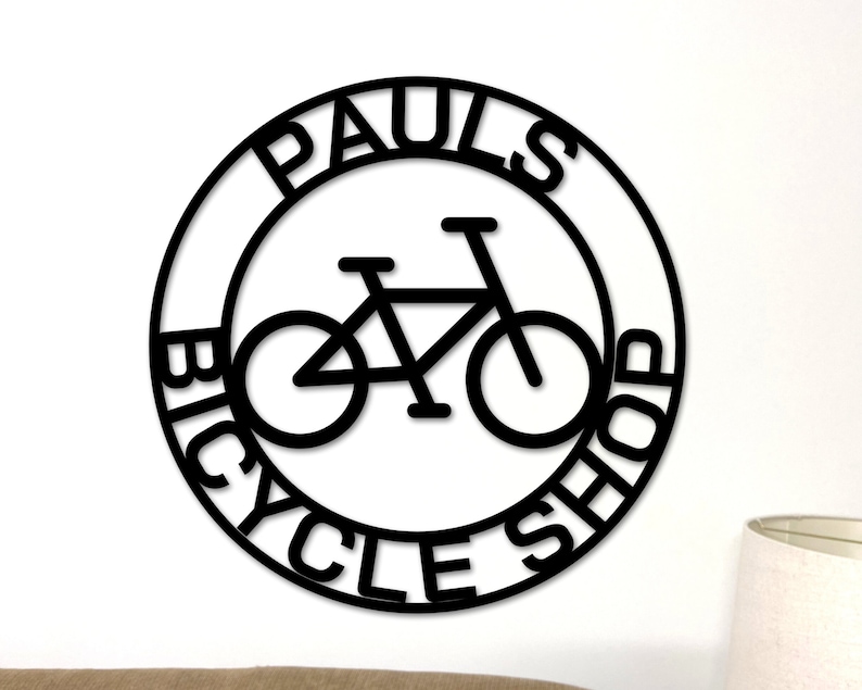 May include: Black and white circular sign with the text "Paul's Bicycle Shop" and a silhouette of a bicycle inside the circle.