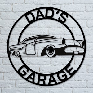 May include: Black metal sign with a circle design. The sign says "Dad's Garage" with a vintage car silhouette inside the circle.