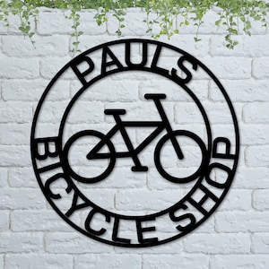 May include: Black metal sign with the words "Paul's Bicycle Shop" in a circle around a silhouette of a bicycle.