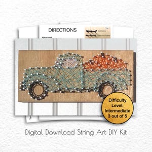 May include: A string art DIY kit featuring a wooden truck carrying pumpkins. The truck is outlined with teal string, and the pumpkins are orange. The kit includes directions and is rated as intermediate, 3 out of 5 in difficulty.
