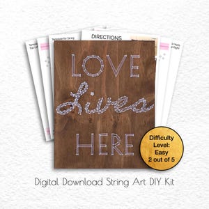 Puede incluir: Un kit de arte de cuerda DIY de descarga digital con la frase "Love Lives Here" sobre un fondo de madera marrón. El kit incluye una plantilla, instrucciones y un nivel de dificultad fácil (2 de 5).