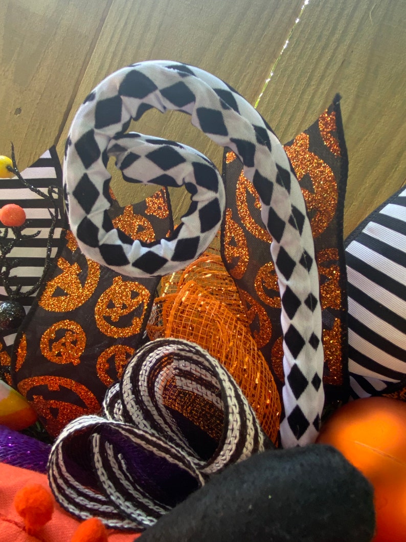 Puede incluir: Una corona de Halloween con cinta a cuadros blanco y negro, cinta de brillo naranja y negro y cinta de malla naranja. La corona tambi&eacute;n tiene cinta a rayas blanco y negro, cinta con estampado de calabaza negro y naranja y un remolino a cuadros blanco y negro.