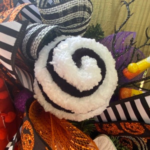 Puede incluir: Una corona de Halloween con cinta a rayas blancas y negras, un remolino blanco y negro, malla naranja y negra y malla morada y negra.
