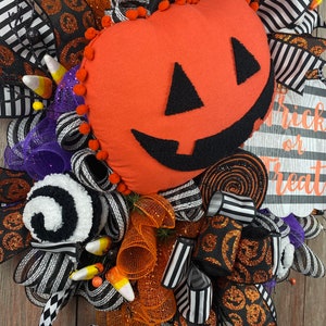 Puede incluir: Corona de Halloween con una cinta a rayas blancas y negras, una cinta de purpurina naranja y negra y una calabaza de fieltro con una cara de jack-o'-lantern. La corona tambi&eacute;n incluye ma&iacute;z dulce, decoraciones de espiral blancas y negras y un letrero que dice "Trick or Treat".