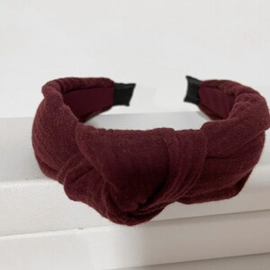 May include: A burgundy knotted headband made of fabric. The headband is a simple design with a single knot in the center.