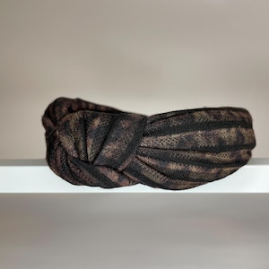 May include: A black and brown patterned knotted headband. The headband is made of a soft, stretchy fabric.