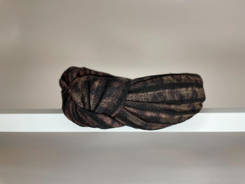 May include: A black and brown patterned knotted headband. The headband is made of a soft, stretchy fabric.