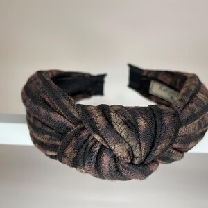 May include: A brown and black knotted headband with a fabric pattern.
