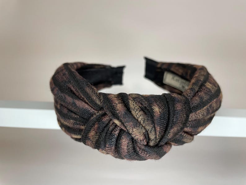 May include: A brown and black knotted headband with a fabric pattern.