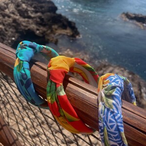 May include: Three colorful fabric headbands with knotted designs. The headbands are blue and green, red and yellow, and blue and white.