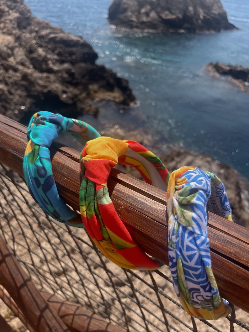 May include: Three colorful fabric headbands with knotted designs. The headbands are blue and green, red and yellow, and blue and white.