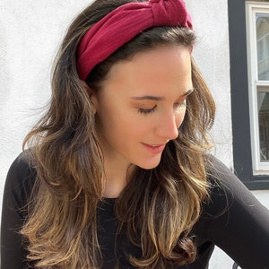 May include: A burgundy knotted headband made of soft fabric. The headband is worn by a person with long brown hair.
