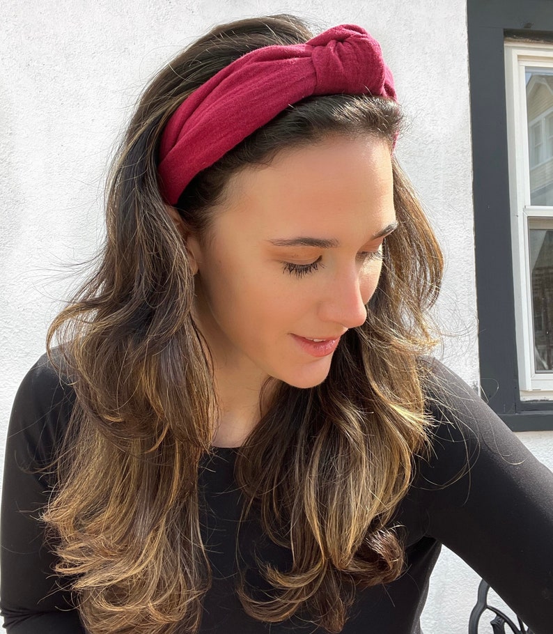 May include: A burgundy knotted headband made of soft fabric. The headband is worn by a person with long brown hair.