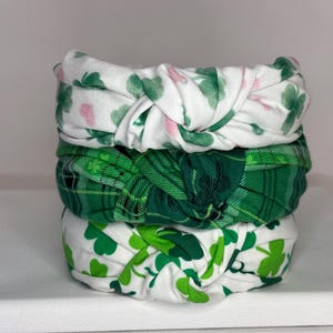 K&ouml;nnte beinhalten: Drei gr&uuml;n-wei&szlig;e gemusterte Stirnb&auml;nder mit einem geknoteten Design. Die Stirnb&auml;nder haben Kleeblatt- und Karomuster.