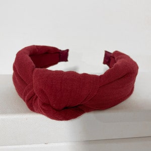 May include: A burgundy knotted headband made of fabric. The headband is a simple design with a single knot in the center.