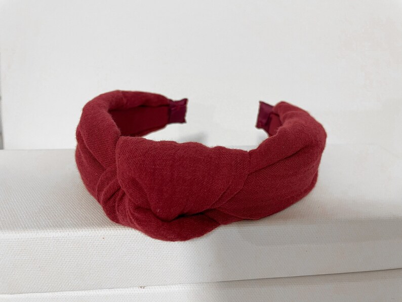 May include: A burgundy knotted headband made of fabric. The headband is a simple design with a single knot in the center.