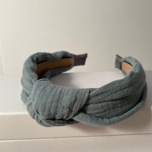 May include: A gray fabric headband with a knotted design. The headband is made of a soft, comfortable material and is perfect for adding a touch of style to any outfit.