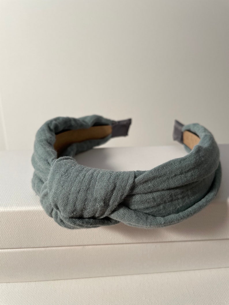 May include: A gray fabric headband with a knotted design. The headband is made of a soft, comfortable material and is perfect for adding a touch of style to any outfit.