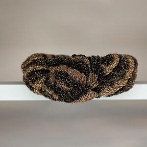 May include: A black and gold knotted headband with a textured, sparkly finish.