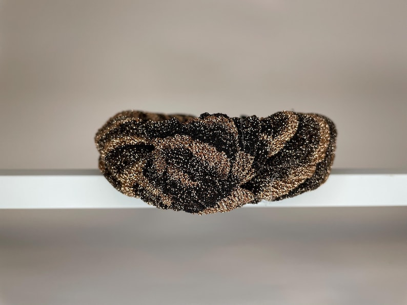 May include: A black and gold knotted headband with a textured, sparkly finish.