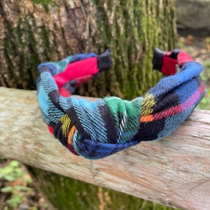 May include: A knotted headband with a plaid pattern in shades of blue, green, red, and yellow. The headband is made of a soft, woven fabric.