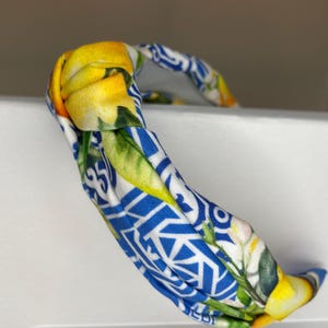 May include: A blue and white headband with a lemon print. The headband is knotted and has a twisted design.