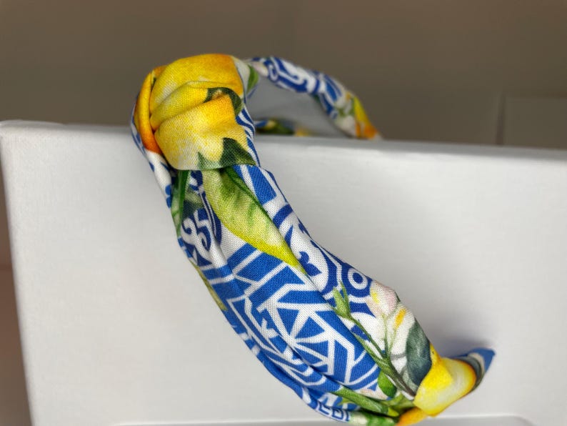 May include: A blue and white headband with a lemon print. The headband is knotted and has a twisted design.