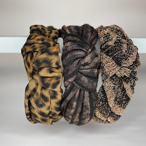 May include: Three fabric headbands in a knotted style. One headband is brown and black with a leopard print, one is black and brown with a swirl pattern, and one is gold and black with a sparkly finish.