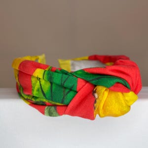 May include: A red, yellow, and green patterned headband with a knotted design.