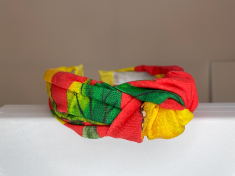 May include: A red, yellow, and green patterned headband with a knotted design.