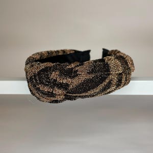 May include: A black and gold knotted headband with a sparkly finish.
