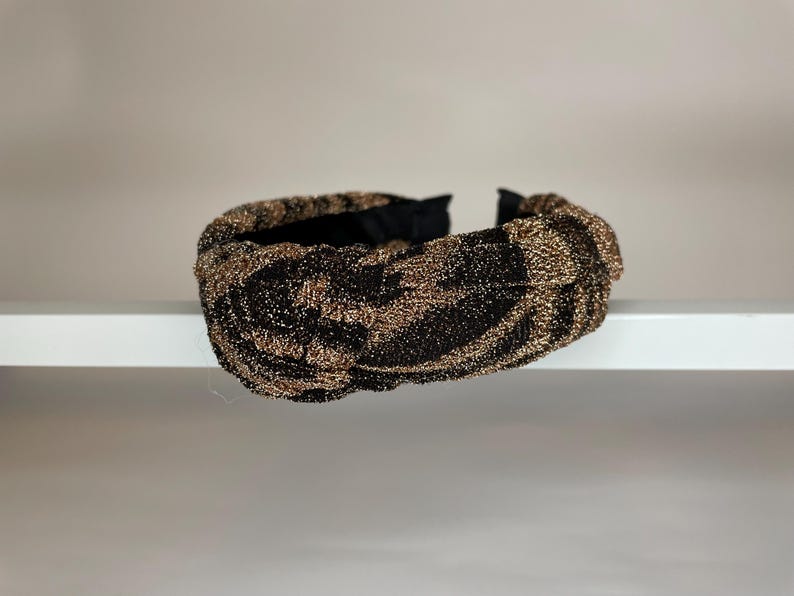 May include: A black and gold knotted headband with a sparkly finish.