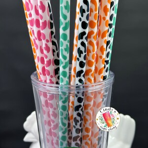 May include: A clear glass with a Starbucks logo on the bottom, filled with a variety of colorful reusable straws with a leopard print design. The straws are in a variety of colors, including pink, green, black, and orange. A sticker with the text "Cindy's Simple Whimsy" is on the side of the glass.