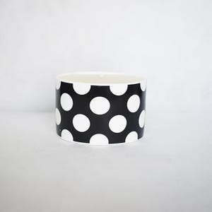 May include: A cylindrical container with a black background and large white polka dots. The container is on a white surface. The inside of the container is white.