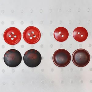 Peut inclure: Divers boutons rouges et marron foncé. Les boutons rouges ont quatre ou deux trous. Les boutons marron foncé sont ronds et ont un aspect légèrement texturé. Les boutons sont disposés sur une surface blanche avec des trous espacés.