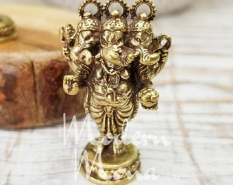 May include: A small, detailed brass statue of a Hindu deity with multiple arms and elephant-like heads. The statue is standing on a round base and has intricate carvings. The overall color is a warm gold.