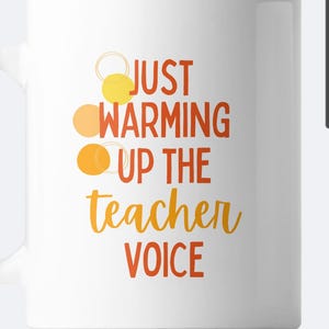 May include: White ceramic mug with the text "Just warming up the teacher voice" in orange and yellow lettering. Three orange and yellow circles are above the text.