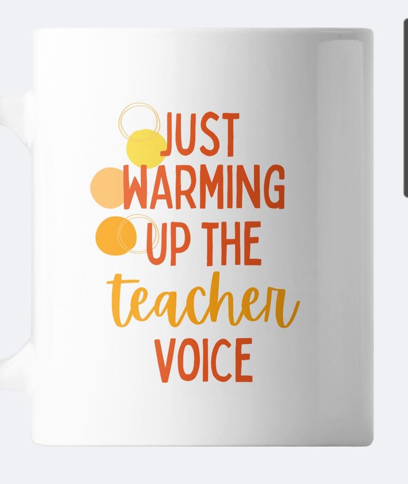 May include: White ceramic mug with the text "Just warming up the teacher voice" in orange and yellow lettering. Three orange and yellow circles are above the text.