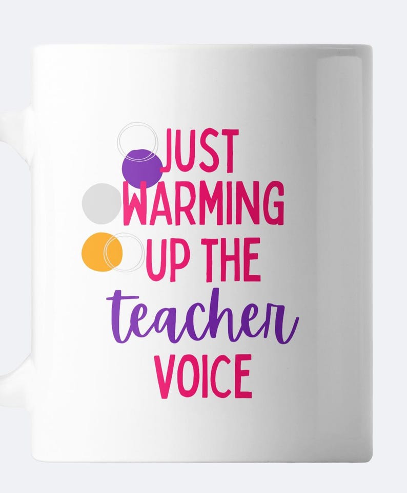 May include: White ceramic mug with the text "Just warming up the teacher voice" in pink and purple lettering. Three colorful circles are arranged vertically on the left side of the mug.