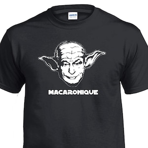 Peut inclure: T-shirt noir avec un dessin blanc d'un visage aux grandes oreilles et le mot "MACARONIQUE" en lettres blanches. Le t-shirt a un col rond et est fait d'une matière douce.