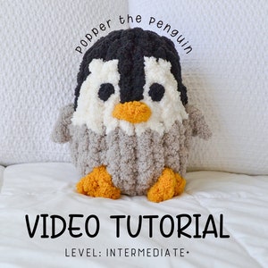 Peut inclure: Un jouet en peluche de pingouin en crochet avec une fourrure noire et blanche, un corps gris et des pieds orange. Le pingouin est assis sur une surface blanche et porte le texte "Popper the penguin" au-dessus de lui. Le texte "VIDEO TUTORIAL" est sous le pingouin et le texte "LEVEL: INTERMEDIATE+" est en dessous.