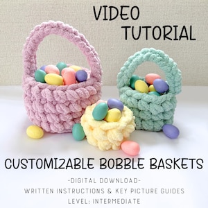 Peut inclure: Trois paniers bobble faits à la main en rose, vert clair et jaune, remplis d'œufs de Pâques colorés. Les paniers ont des anses et sont faits d'un fil épais et texturé. Le texte sur l'image indique "VIDEO TUTORIAL" et "CUSTOMIZABLE BOBBLE BASKETS".
