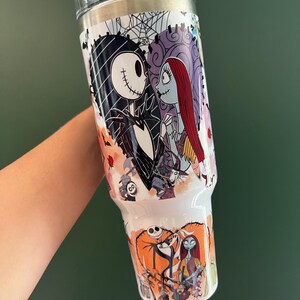 K&ouml;nnte beinhalten: Ein wei&szlig;er Becher mit Jack Skellington und Sally aus The Nightmare Before Christmas. Das Design umfasst einen herzf&ouml;rmigen Hintergrund mit einem Spinnennetz, Rosen und anderen Charakteren. Der Becher hat einen wei&szlig;en Deckel und einen silbernen Rand.