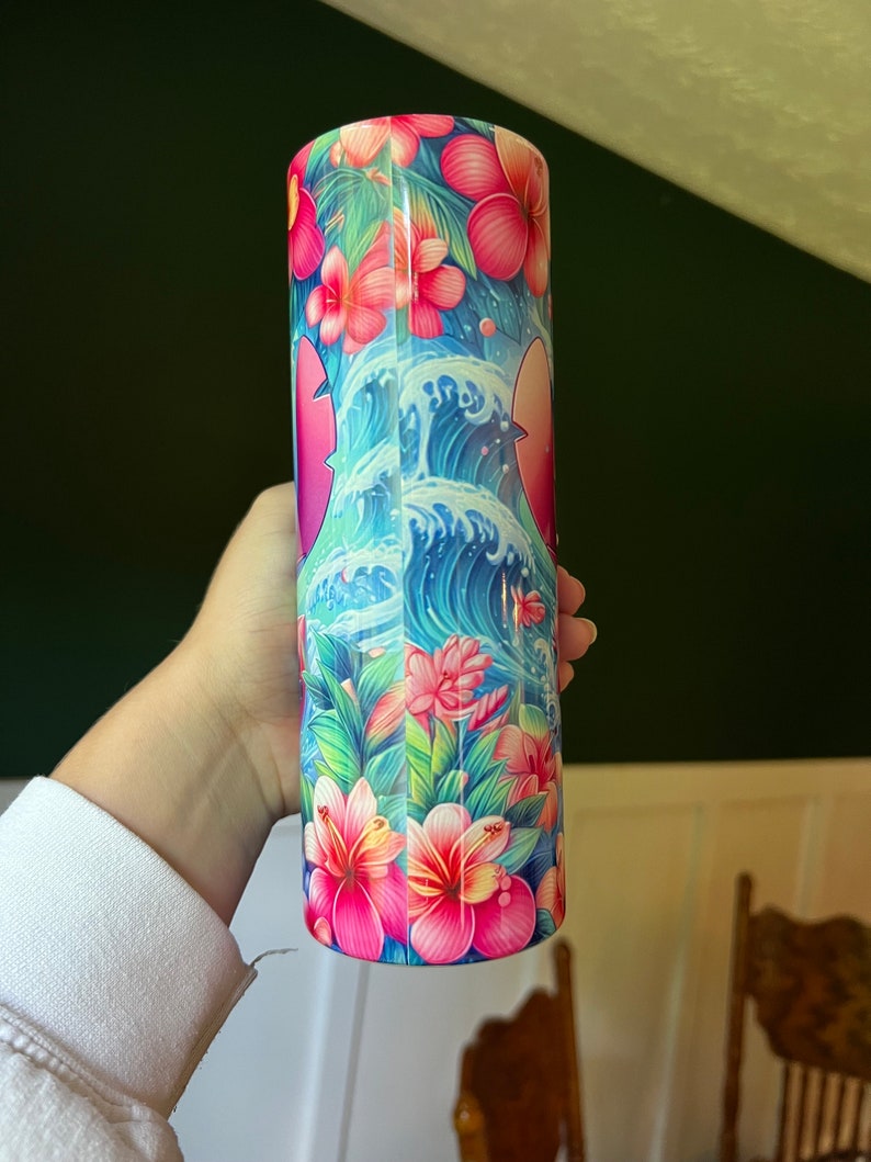 Puede incluir: Un vaso de acero inoxidable con un dise&ntilde;o tropical colorido. El dise&ntilde;o presenta flores rosas, hojas verdes y olas azules.