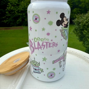 May include: White tumbler with a white lid, featuring cartoon characters and the text "Astro Blasters" in pink and green. The tumbler includes a bamboo lid and a straw.